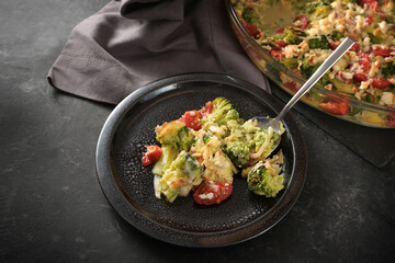Healthy vegetarian low carb meal, casserole from vegetables with broccoli, tomatoes, onions, feta and cheese, on a dark plate and a gray slate table, copy space, selected focus