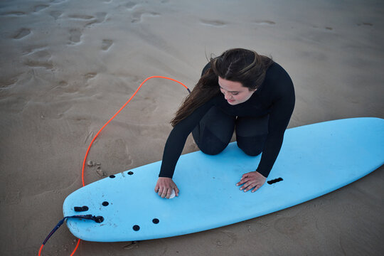 Female Overweight Surfer Waxing Board With Pleasure Smile At The Ocean Cloudy Beach