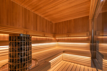 A spacious sauna made of light wood. Wide benches, soft lighting, heating element with .stones.