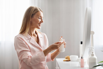 Beautiful mature lady applying makeup remover lotion on cotton pad at home