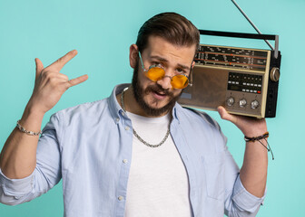 Young lebanese man using retro tape record player to listen music, disco dancing of favorite track, having fun, entertaining, fan of vintage technologies. Arabian guy isolated on blue background