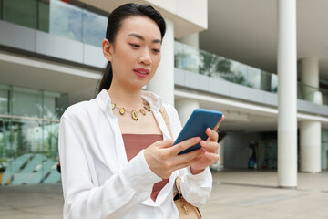 Cheerful business woman reading text messages from her coworker when standing outdoors