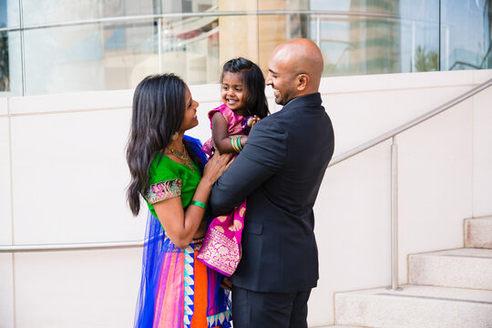 beautiful indian family with daughter girl hugging and smiling with a bindi and traditional sari dress in front of a building with staircase