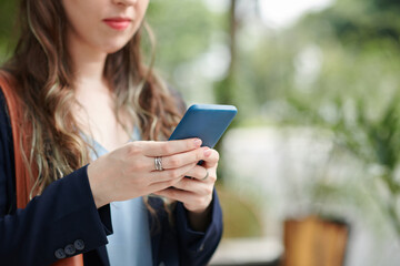 Cropped image of serious businesswoman answering text messages from coworker or reading notifications