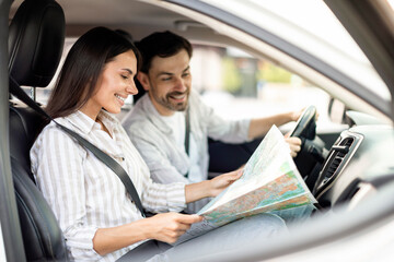 Travel concept. Happy couple using map in car