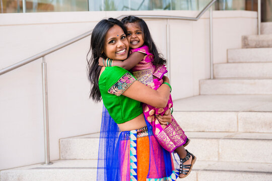 beautiful indian family mom mother with daughter girl hugging and smiling with a bindi and traditional sari dress in front of a building with staircase