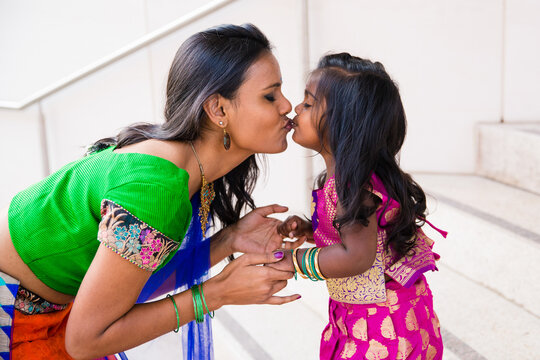 beautiful indian family mom mother with daughter girl holding hands and kissing with a bindi and traditional sari dress in front of a building with staircase