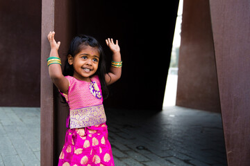 close up of little indian girl wearing a sari and bindi and traditional bracelets jewelry in front of a rust wall