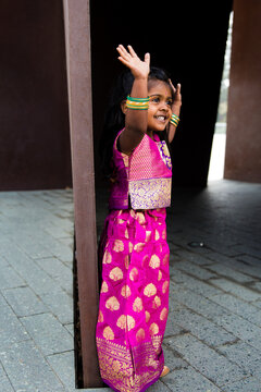 close up of little indian girl wearing a sari and bindi and traditional bracelets jewelry in front of a rust wall