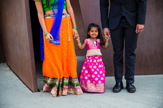 close up of little indian girl wearing a sari and bindi holding hands with her mom and dad and smiling