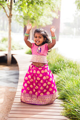 close up of little indian girl wearing a sari and bindi and traditional bracelets jewelry in front of trees and greenery