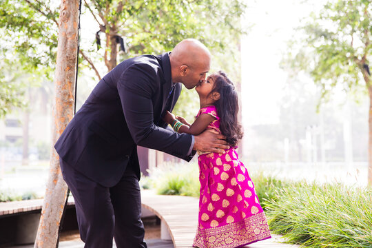 beautiful indian family dad father with daughter girl kissing and smiling with a bindi and traditional sari dress in front of trees and greenery