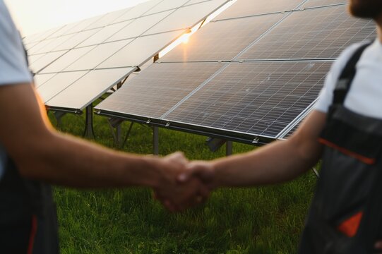 Workers shaking hands on a background of solar panels on solar power plant.