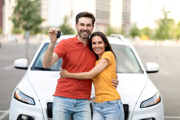 Young joyful man and woman standing near new car outdoors