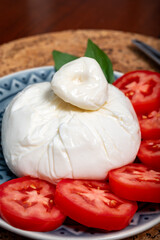 Fresh handmade soft Italian cheese from Puglia, white ball of burrata foglia saporosa or burratina cheese made from mozzarella and cream filling served with tomatoes and fresh basil