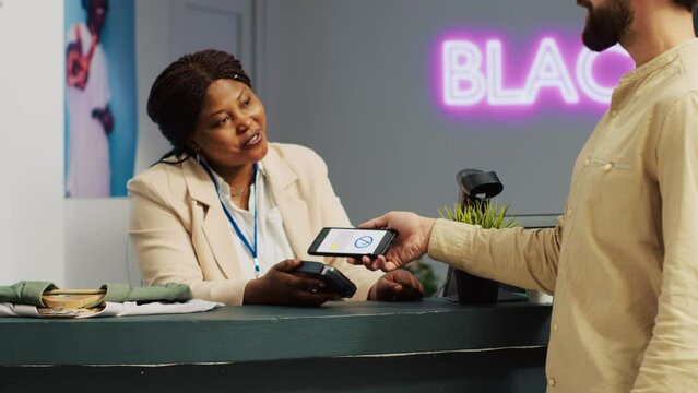 Client making pos contactless payment while he is shopping for clothes in retail store. Young adult shopper at clothing outlet checkout counter using mobile ngc concept to pay. Handheld shot.