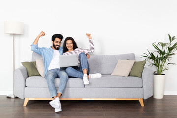 Excited eastern couple raising hands up, shopping online at home