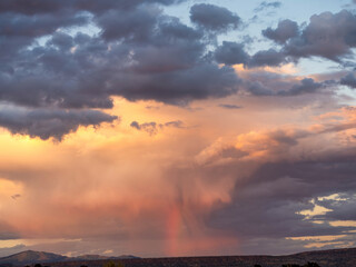 Dramatic sunset with a supercell monsoon rainstorm and a rainbow in the New Mexico landscape.