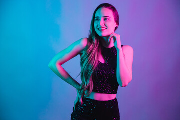 Model on blue and pink neon background posing for photo. smiling with hand on chin.