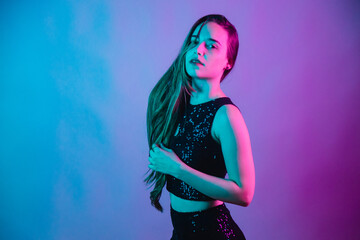 Model on blue and pink neon background posing for photo. staring at the camera with a hand in her hair.