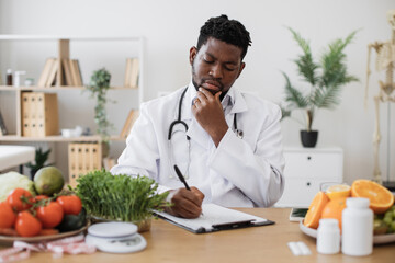 Doctor gastroenterologist filling patient's case history and prescribing recipe wile sitting at work desk full of fruits and vegetables. Male professional writing vegetable diet plan in clinics.