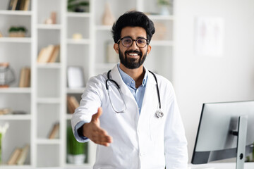 Friendly handsome middle eastern doctor outstretching hand and smiling - obrazy, fototapety, plakaty