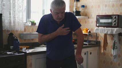 Sickly senior man experiencing a heart attack with chest palpitations at home by kitchen sink. Medically ill elderly person needing emergency aid