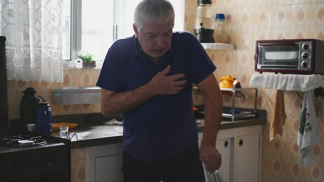 Sickly senior man experiencing a heart attack with chest palpitations at home by kitchen sink. Medically ill elderly person needing emergency aid