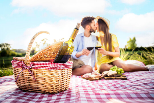 Young couple in love having picnic in the countryside field - Beautiful boyfriend and girlfriend enjoying wine taste experience - Food and beverage life style concept