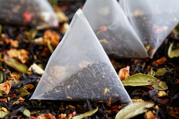 Triangular pyramidal tea bags filled with flavored black tea, with fruits, berries and flowers, lie...