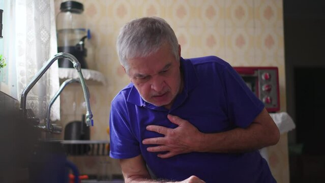 Senior man suffering heart attack at home by kitchen sink and falling to the floor. Distressed Elderly person collapsing in pain to the ground alone in residence