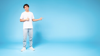 Chinese guy pointing aside gesturing thumbs up on blue background