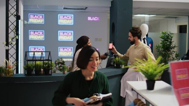 Mobile coupon marketing in retail shop. Client showing smartphone with black friday promo code to cashier, preparing to buy clothes at promotional prices. Shopper using loyalty voucher.