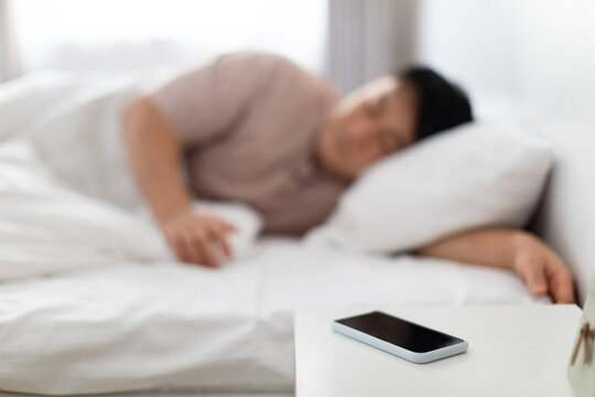 Selective focus on smartphone on bedside near asian man sleeping