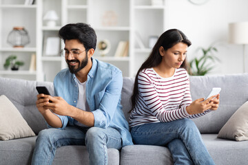 Young indian wife and husband using mobile phones at home