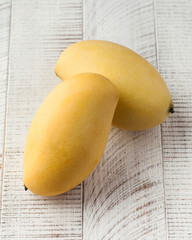 Two ripe yellow mangoes on a white wooden background. Tropical fruits.