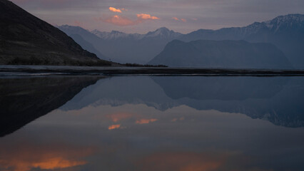View of sun setting in the back of mountains and reflecting in the surface of a river around Skardu, Gilgit Baltistan in the Karakoram range of the Himalayas.