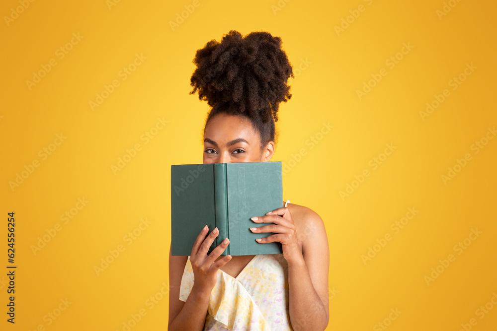 Wall mural cheerful young black woman reading book, has fun alone