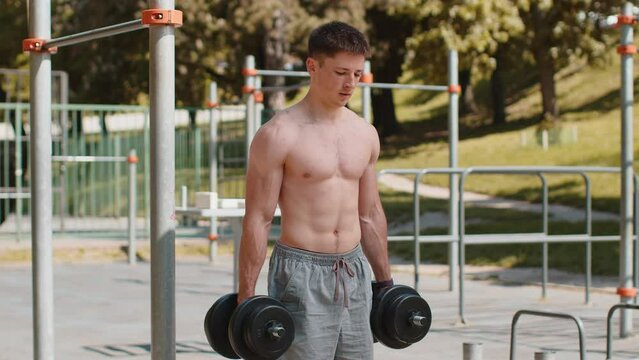Athletic caucasian topless muscular man doing arms weight lifting dumbbells exercises, pumping up arm bicep muscles. Young guy on playground. Sports health fitness routine workout. Strength motivation