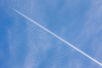 Airplane and contrails or vapour trails after a large commercial jet plane high in sky, Diagonal trace of plane flying in clear blue sky, Aircraft waste smoke trails, Air transport background.