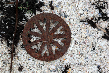 Rusty round detail on white coral sand, debris on the shore of the fjord, steampunk
