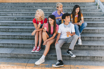Group of sad, unhappy friends, multiracial teenagers eating ice cream, drinking lemonade sitting on...