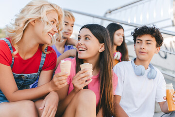 Group of smiling friends, multiracial teenagers eating ice cream, drinking lemonade sitting...
