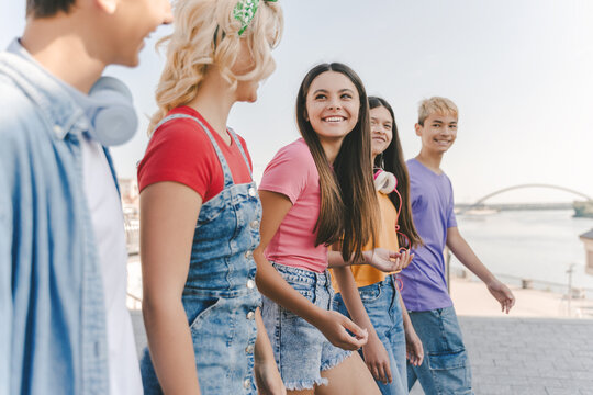 Group of smiling friends, multiracial teenagers wearing colorful casual clothes talking, walking on the street. Happy stylish boys and girls outdoors. Friendship, positive lifestyle, summer concept 
