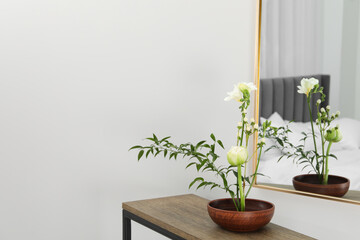 Stylish ikebana with beautiful flowers and green branch carrying cozy atmosphere at home, space for text