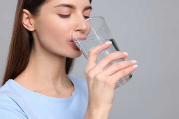 Healthy habit. Woman drinking fresh water from glass on grey background
