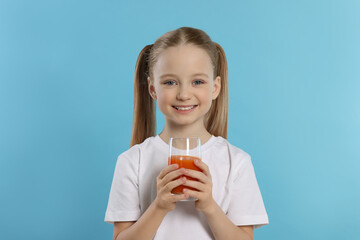 Cute little girl with glass of fresh juice on light blue background