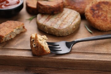 Fototapeta na wymiar Fork with piece of delicious vegan cutlet on wooden table, closeup