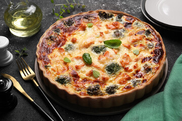 Delicious homemade salmon quiche with broccoli and cutlery on black table