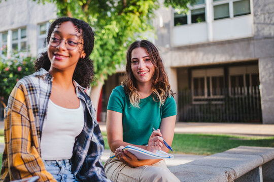 Portrait of a smiling college student girl looking at camera. She is holding a notebook and a pen.